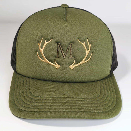 Frontale Aufnahme von einer Olivgrünen Baseball Trucker-Cap mit einem Hirschgeweih und Initialen bestickt auf einem weißen Hintergrund
