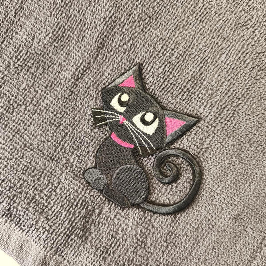 Gestickter Aufnäher mit einer stilisierten schwarzen Katze mit rosa Akzenten an Ohren und Halsband. Die Katze hat weiße Schnurrhaare und große Augen. Zum Aufnähen auf Textilien.