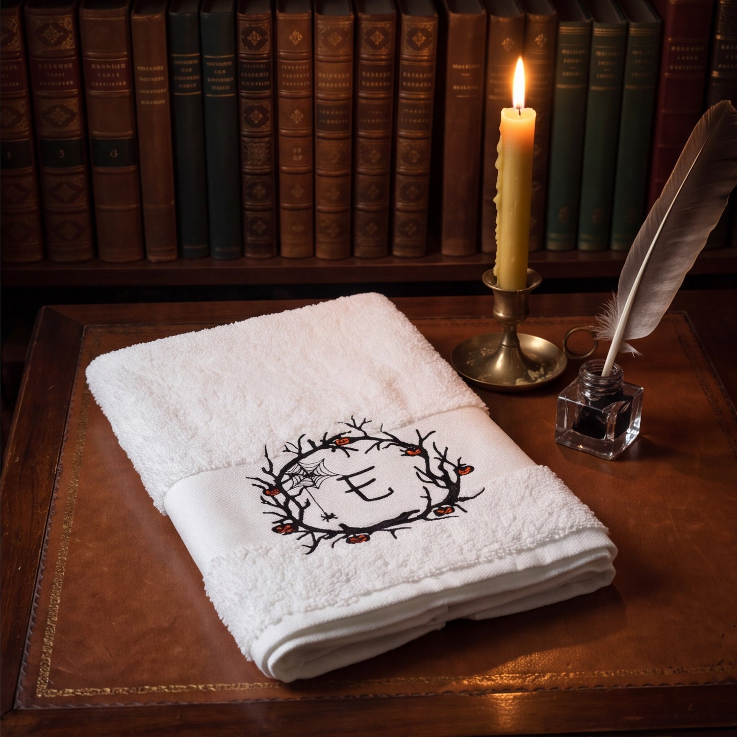 Personalisiertes weißes Handtuch mit bestickter Initiale E im Halloween Spuk-Kranz auf einem dunkelbraunen Tisch mit Bücher und Schreibware sowie einer brennenden Kerze.