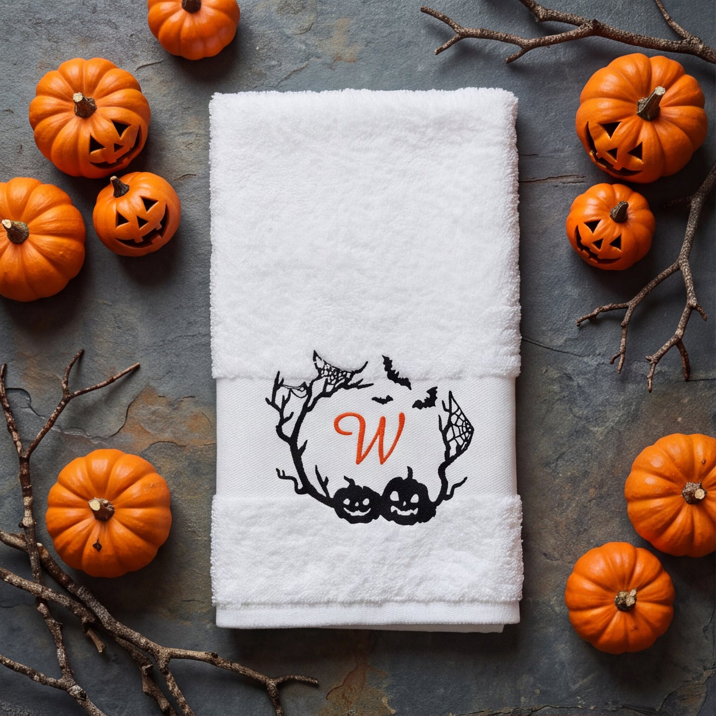 Weißes Halloween-Handtuch mit besticktem Monogramm W im Fledermaus- und Kürbis-Kranz, umringt von Deko-Kürbissen