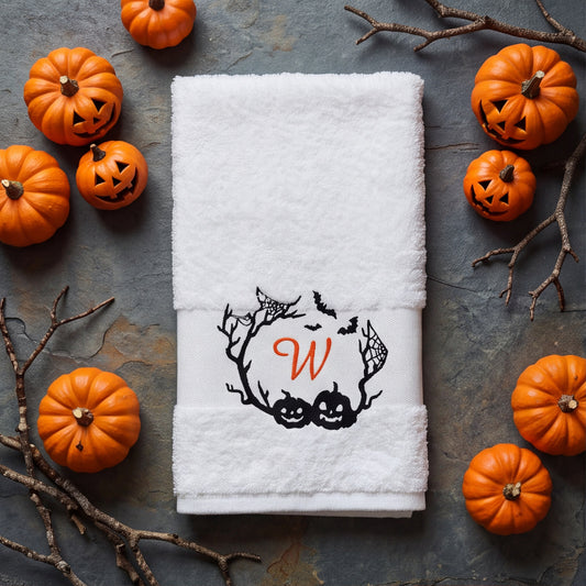 Weißes Halloween-Handtuch mit besticktem Monogramm W im Fledermaus- und Kürbis-Kranz, umringt von Deko-Kürbissen