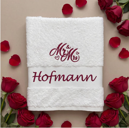 Weißes Handtuch bestickt mit weinrotem Mr & Mrs Signet und Nachnamen Hofmann, umringt von roten Rosen