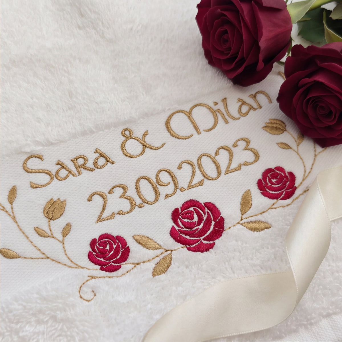 Nahaufnahme der hochwertigen goldenen Garnstickerei Sara & Milan 23.09.2023 und der roten Stickrosen auf flauschigem Baumwollstoff.
