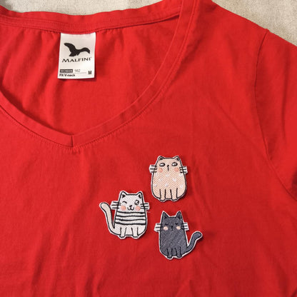 Eine Beispielaufnahme von drei verschiedenen Katzen-Aufnäher auf einem roten T-Shirt.