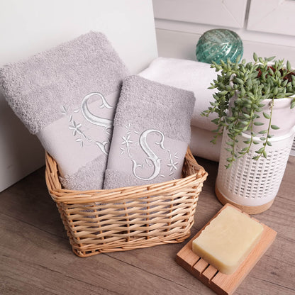 Könnte beinhalten: Zwei graue Handtücher mit gestickten Blumenmustern und dem Buchstaben "S" in einem Weidenkorb. Eine Seife liegt auf einem Seifenspender aus Holz neben dem Korb.